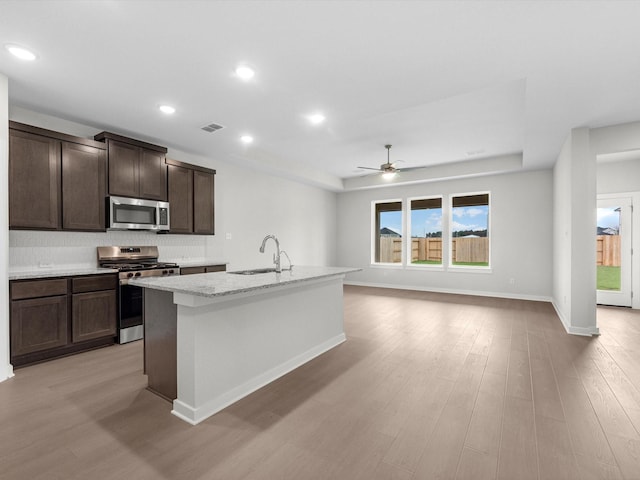 kitchen with appliances with stainless steel finishes, sink, light hardwood / wood-style floors, an island with sink, and dark brown cabinets