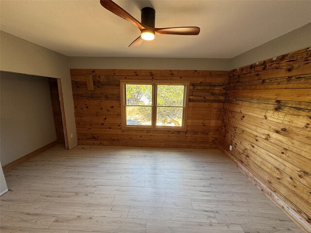 empty room with light hardwood / wood-style flooring, ceiling fan, and wood walls