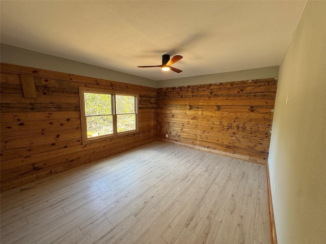 unfurnished room with a textured ceiling, light hardwood / wood-style floors, ceiling fan, and wood walls