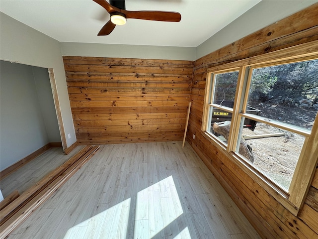 empty room featuring ceiling fan, wood walls, and light wood-type flooring