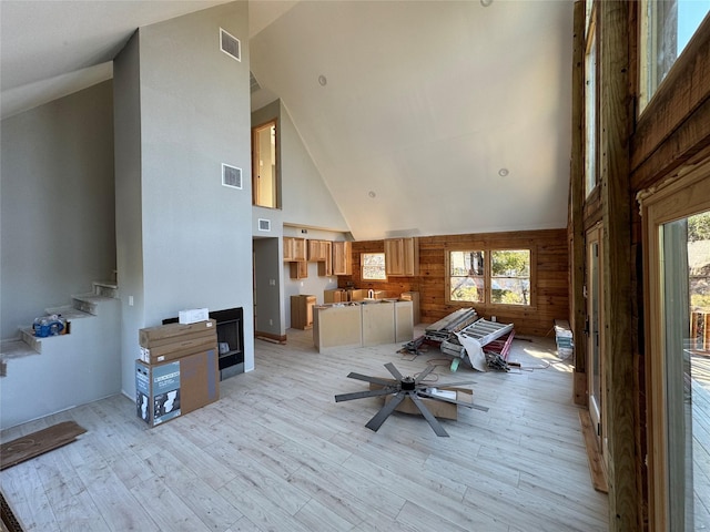 interior space with wooden walls, high vaulted ceiling, and light hardwood / wood-style flooring