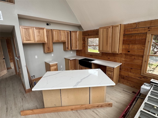 kitchen with vaulted ceiling, a kitchen island, light hardwood / wood-style flooring, and wood walls