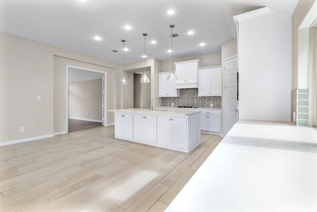 kitchen with white cabinets, light wood-type flooring, decorative light fixtures, and a center island with sink