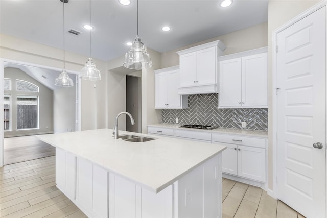 kitchen featuring white cabinetry, sink, hanging light fixtures, and an island with sink