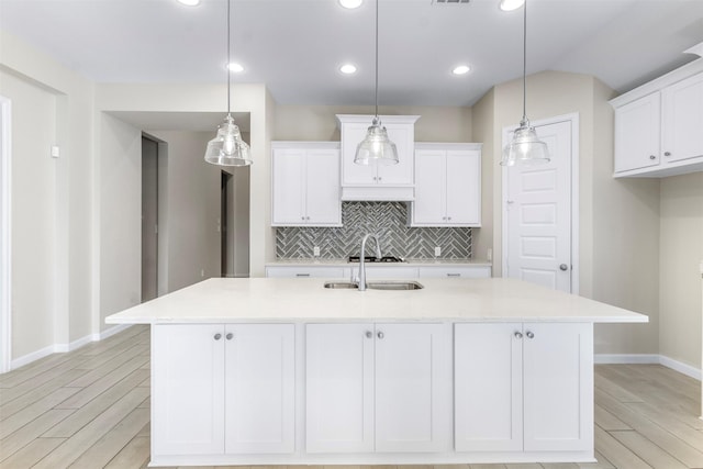 kitchen featuring white cabinetry, a center island with sink, pendant lighting, and light hardwood / wood-style floors