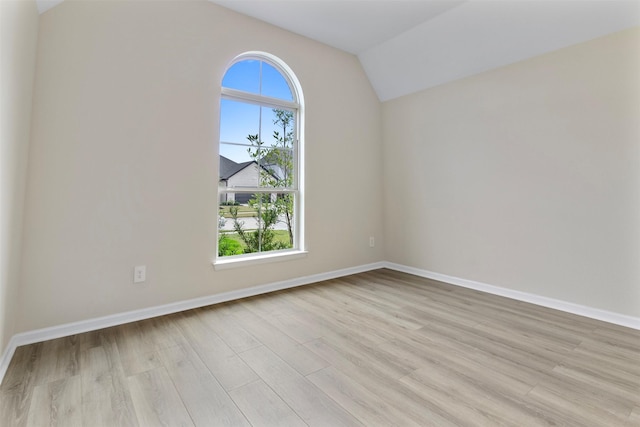 spare room featuring light wood-type flooring and vaulted ceiling