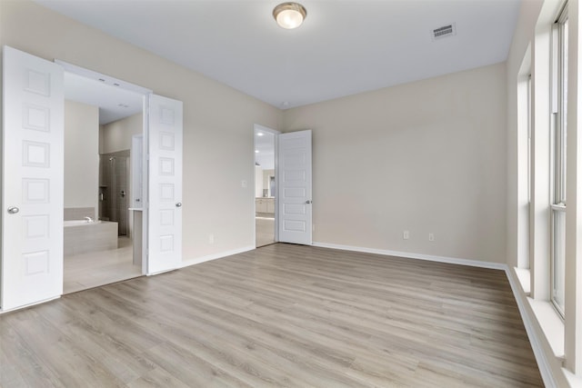 unfurnished bedroom with light wood-type flooring, ensuite bath, and multiple windows