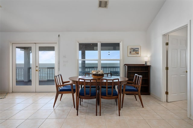 tiled dining room featuring plenty of natural light, a water view, lofted ceiling, and french doors