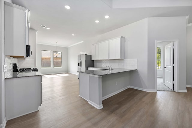 kitchen with kitchen peninsula, light wood-type flooring, tasteful backsplash, stainless steel appliances, and white cabinetry