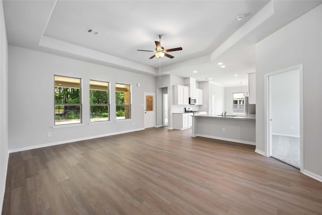 unfurnished living room featuring hardwood / wood-style floors, a tray ceiling, ceiling fan, and sink