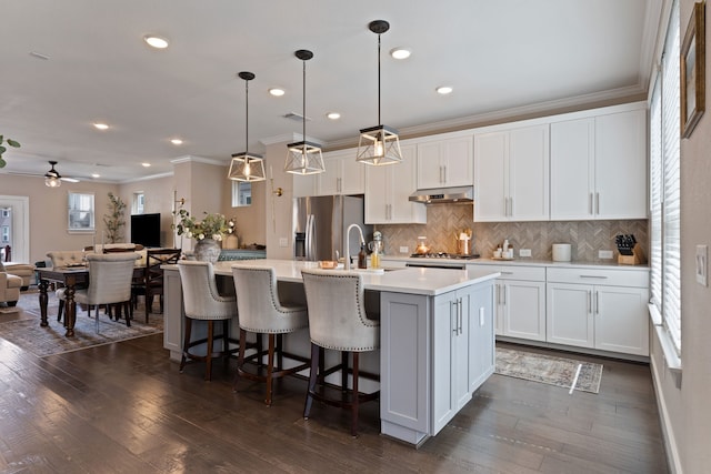 kitchen featuring a kitchen island with sink, dark wood-type flooring, hanging light fixtures, appliances with stainless steel finishes, and white cabinetry