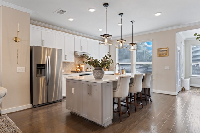 kitchen with a healthy amount of sunlight, stainless steel fridge with ice dispenser, white cabinetry, and a kitchen island with sink