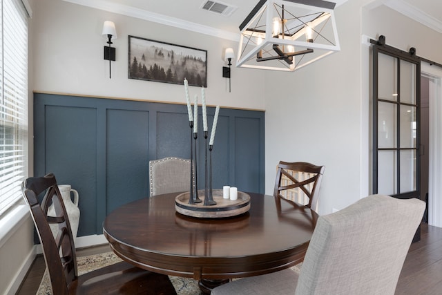 dining area featuring dark hardwood / wood-style floors, a barn door, ornamental molding, and a chandelier