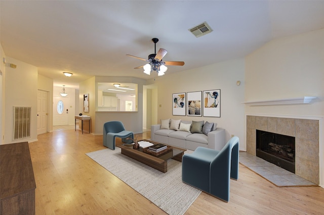 living room with a tiled fireplace, ceiling fan, and light hardwood / wood-style flooring