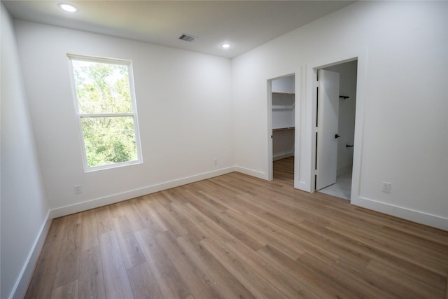 unfurnished bedroom featuring light wood-type flooring, a walk in closet, a closet, and connected bathroom