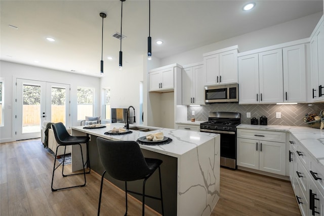 kitchen with sink, hardwood / wood-style floors, pendant lighting, a center island with sink, and appliances with stainless steel finishes