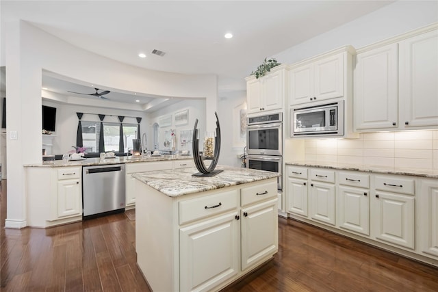 kitchen featuring light stone countertops, stainless steel appliances, ceiling fan, dark hardwood / wood-style floors, and a kitchen island