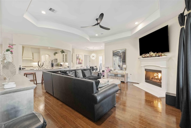 living room with hardwood / wood-style floors, ceiling fan with notable chandelier, and a tray ceiling