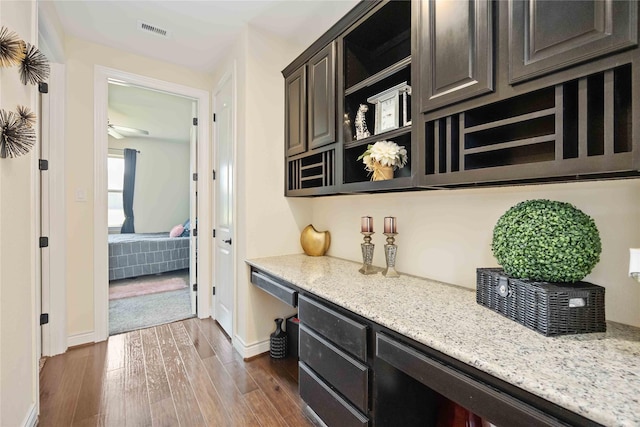 bar featuring light stone countertops, dark hardwood / wood-style flooring, dark brown cabinetry, ceiling fan, and built in desk