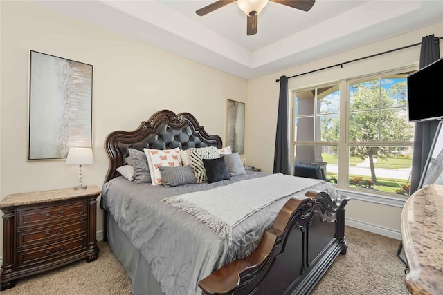 bedroom with a raised ceiling, ceiling fan, and light colored carpet