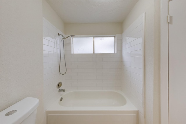 bathroom featuring toilet, a textured ceiling, and tiled shower / bath