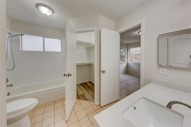 full bathroom featuring tile patterned floors, vanity, a textured ceiling, toilet, and tiled shower / bath