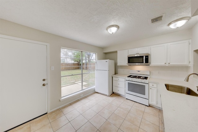 kitchen with white cabinets, light tile patterned floors, white appliances, and sink