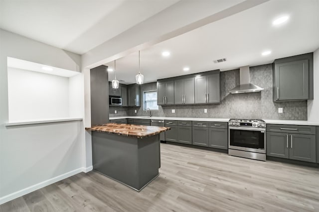 kitchen with light wood-type flooring, wall chimney range hood, sink, and appliances with stainless steel finishes