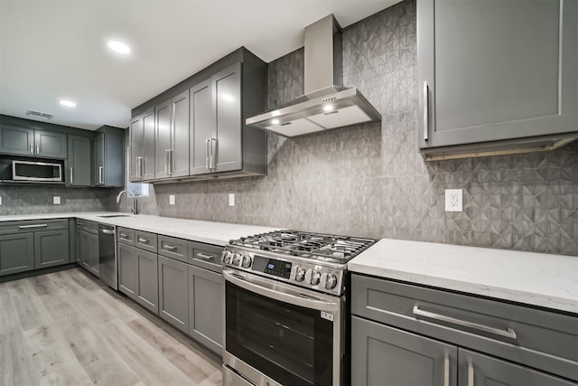 kitchen with light stone countertops, wall chimney exhaust hood, stainless steel appliances, backsplash, and light hardwood / wood-style floors