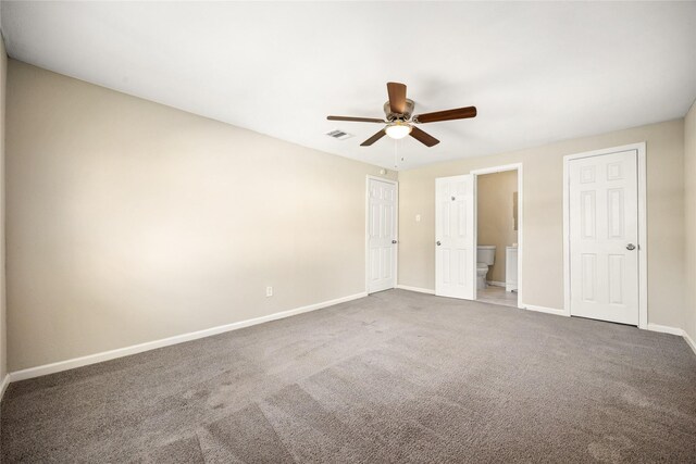 unfurnished bedroom with ceiling fan, ensuite bathroom, and dark carpet