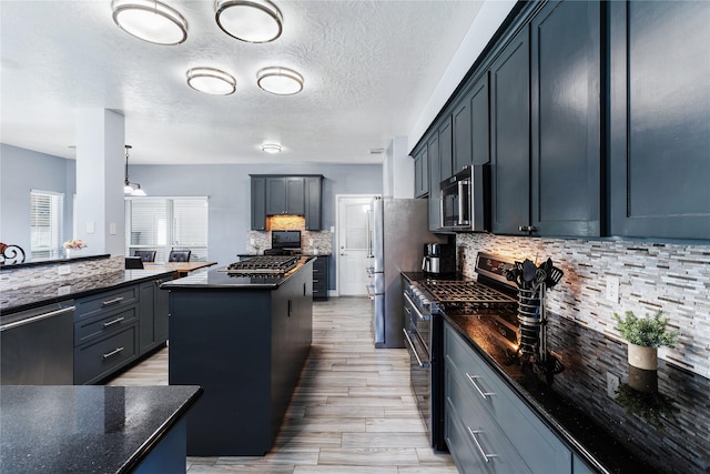 kitchen with pendant lighting, a center island, a textured ceiling, appliances with stainless steel finishes, and light hardwood / wood-style floors