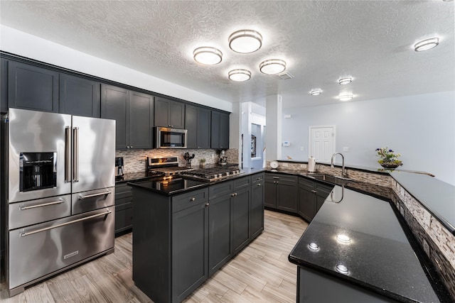 kitchen with a textured ceiling, stainless steel appliances, sink, a center island, and light hardwood / wood-style floors