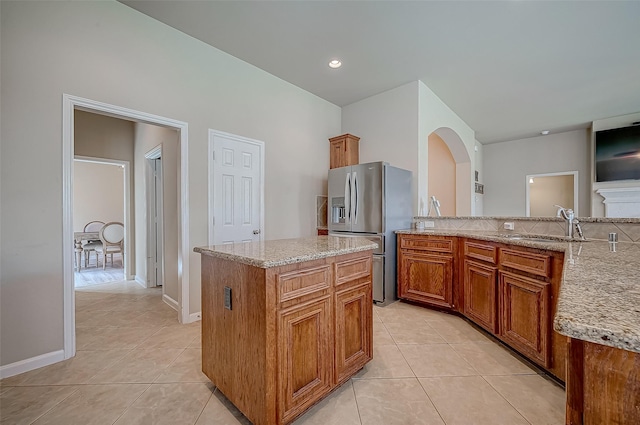 kitchen featuring a center island, light stone countertops, stainless steel fridge with ice dispenser, and light tile patterned flooring