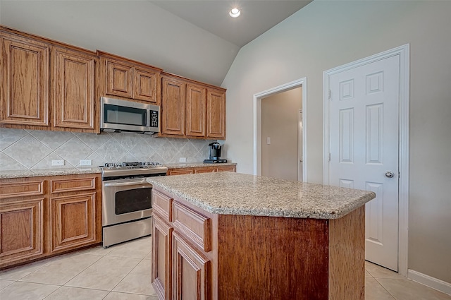 kitchen featuring stainless steel appliances, a kitchen island, backsplash, vaulted ceiling, and light tile patterned flooring