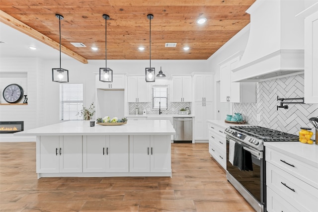 kitchen with pendant lighting, custom exhaust hood, a center island, appliances with stainless steel finishes, and light hardwood / wood-style floors