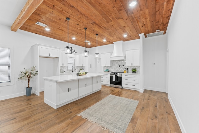 kitchen with stainless steel range, a center island, white cabinets, custom exhaust hood, and light wood-type flooring