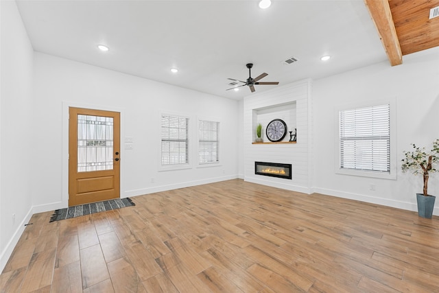 unfurnished living room featuring beamed ceiling, ceiling fan, light hardwood / wood-style floors, and a fireplace