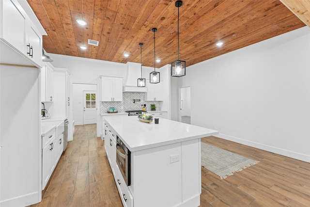 kitchen featuring pendant lighting, a center island, premium range hood, white cabinets, and light hardwood / wood-style floors