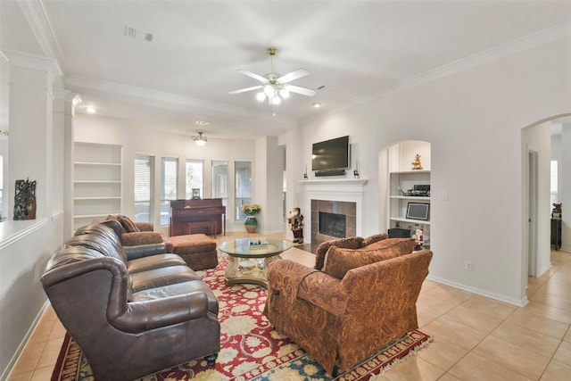 living room featuring crown molding, built in shelves, a tile fireplace, and light tile patterned flooring