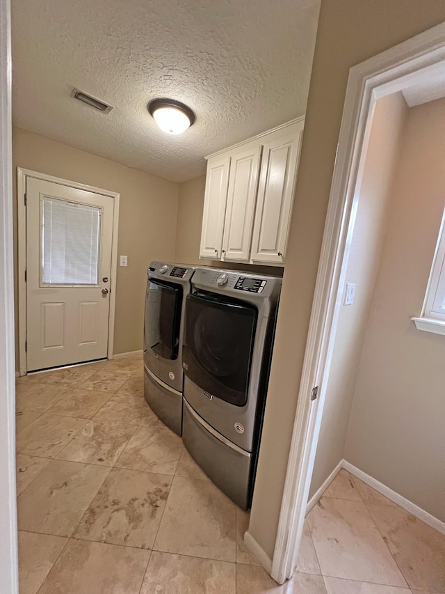 washroom featuring cabinets, washing machine and dryer, and a textured ceiling