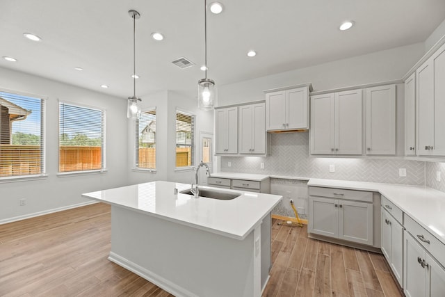 kitchen with a center island with sink, sink, gray cabinets, tasteful backsplash, and decorative light fixtures