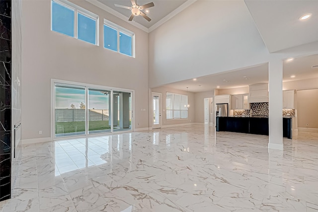 unfurnished living room featuring ceiling fan, a towering ceiling, and ornamental molding