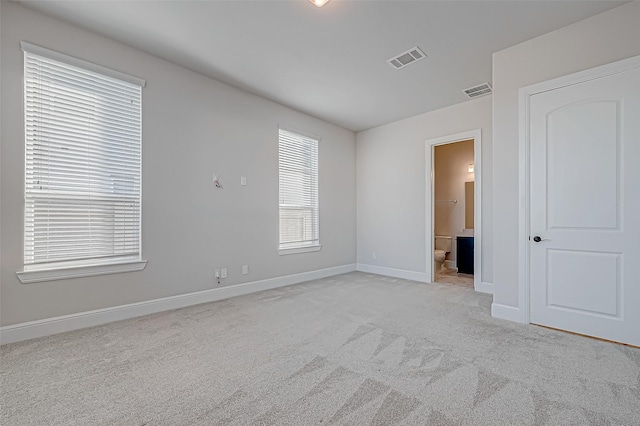 unfurnished bedroom featuring light carpet and ensuite bath