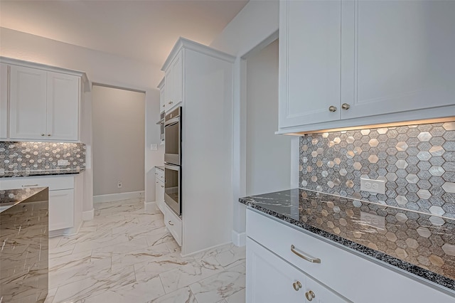 kitchen featuring dark stone countertops, backsplash, white cabinets, and stainless steel double oven