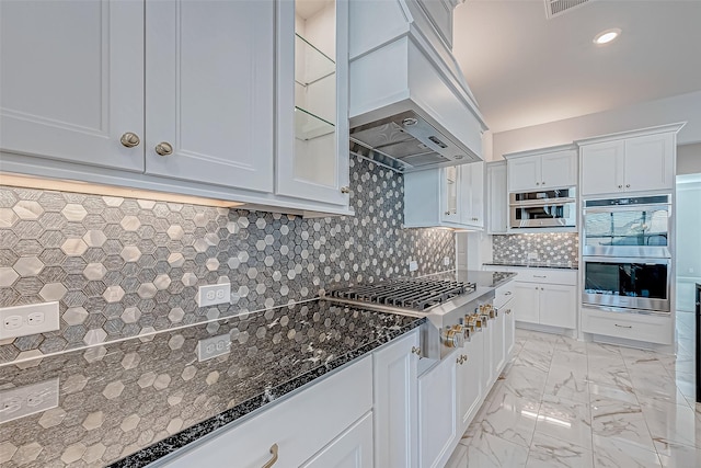 kitchen with backsplash, dark stone countertops, custom exhaust hood, stainless steel appliances, and white cabinets