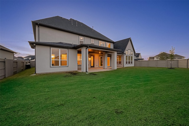 back house at dusk with a patio area and a yard