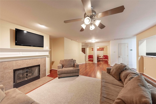 living room featuring ceiling fan, a tiled fireplace, and hardwood / wood-style floors