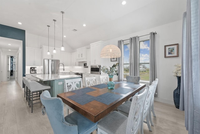 dining area with lofted ceiling, sink, and light hardwood / wood-style flooring