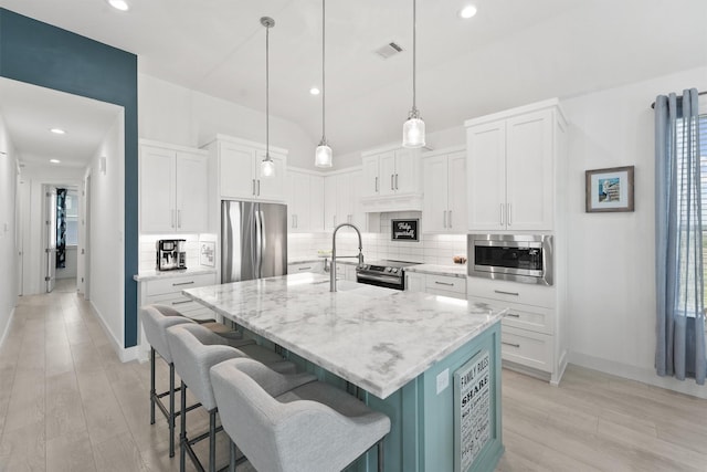 kitchen featuring appliances with stainless steel finishes, pendant lighting, a center island with sink, white cabinets, and light hardwood / wood-style floors