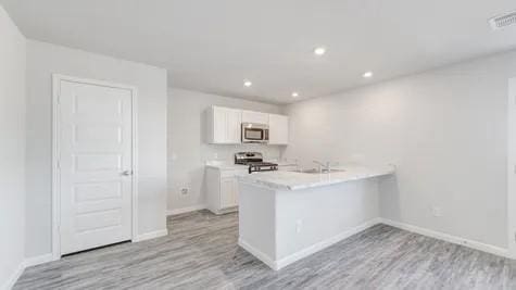 kitchen with kitchen peninsula, appliances with stainless steel finishes, light wood-type flooring, sink, and white cabinets